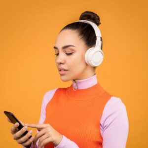 Woman wearing headphones and using smartphone against orange background.