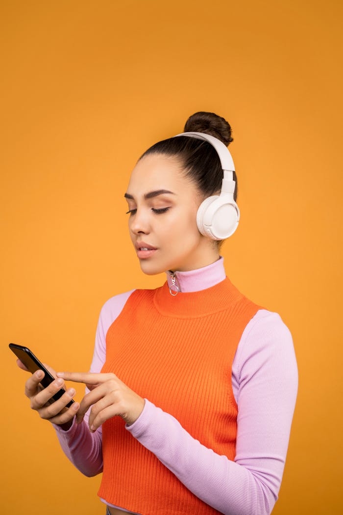 Woman wearing headphones and using smartphone against orange background.