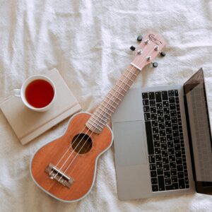 A cozy composition featuring a ukulele, laptop, and cup of tea on a bed for a relaxing indoor ambiance.