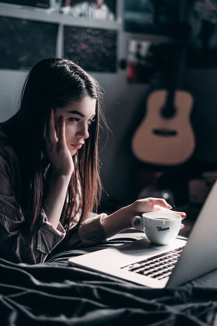 gallery-03 Woman lying on bed, focused on laptop with a coffee cup in hand, embracing remote work lifestyle.