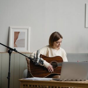 Adult woman playing guitar with laptop for online music learning. Indoors, cozy setting.