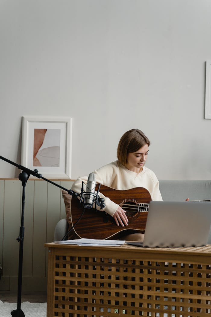 services-03 Adult woman playing guitar with laptop for online music learning. Indoors, cozy setting.