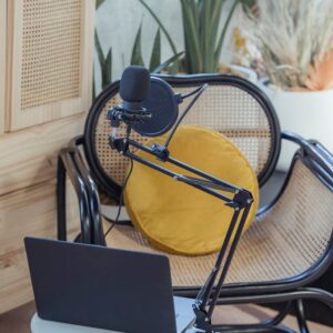 Modern laptop and microphone on tripod placed near wicker chair in modern studio before recording podcast