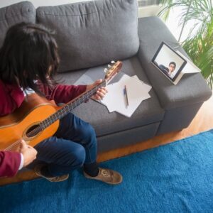 A man learning guitar online at home using an acoustic guitar and tablet.