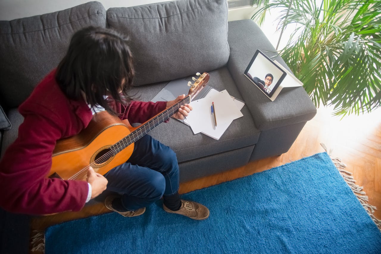 services-01 A man learning guitar online at home using an acoustic guitar and tablet.