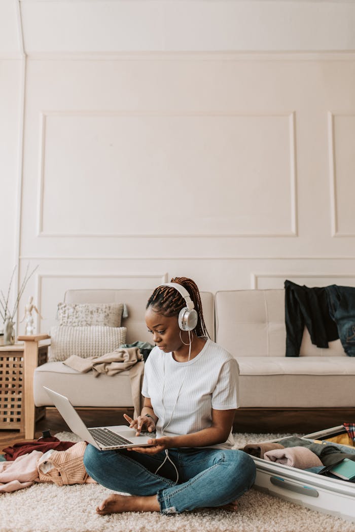 gallery-05 Young woman with braided hair sitting cross-legged, working on a laptop and listening to music in a cozy living room.